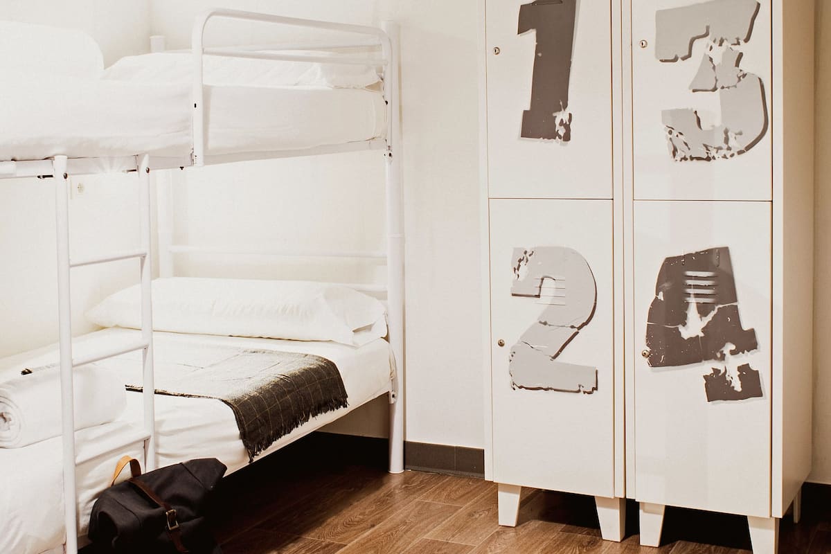 Ein Stockbett, ein Rucksack auf dem Boden, ein weißer Schrank mit Türnummern und Holzboden.