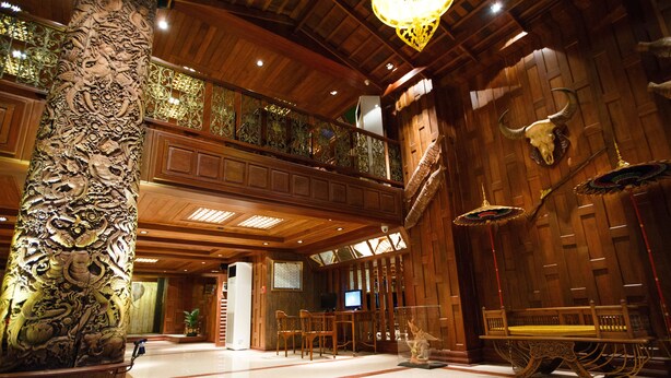 Un vestíbulo espacioso con techo alto, columnas de madera ornamentadas, una gran decoración de cráneo de toro y una mesa de madera tradicional.