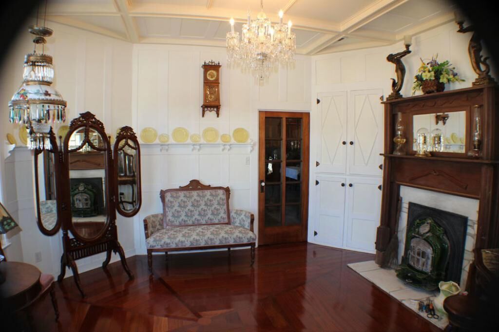 A room with a wooden floor, a sofa, a fireplace, a mirror, and a chandelier.