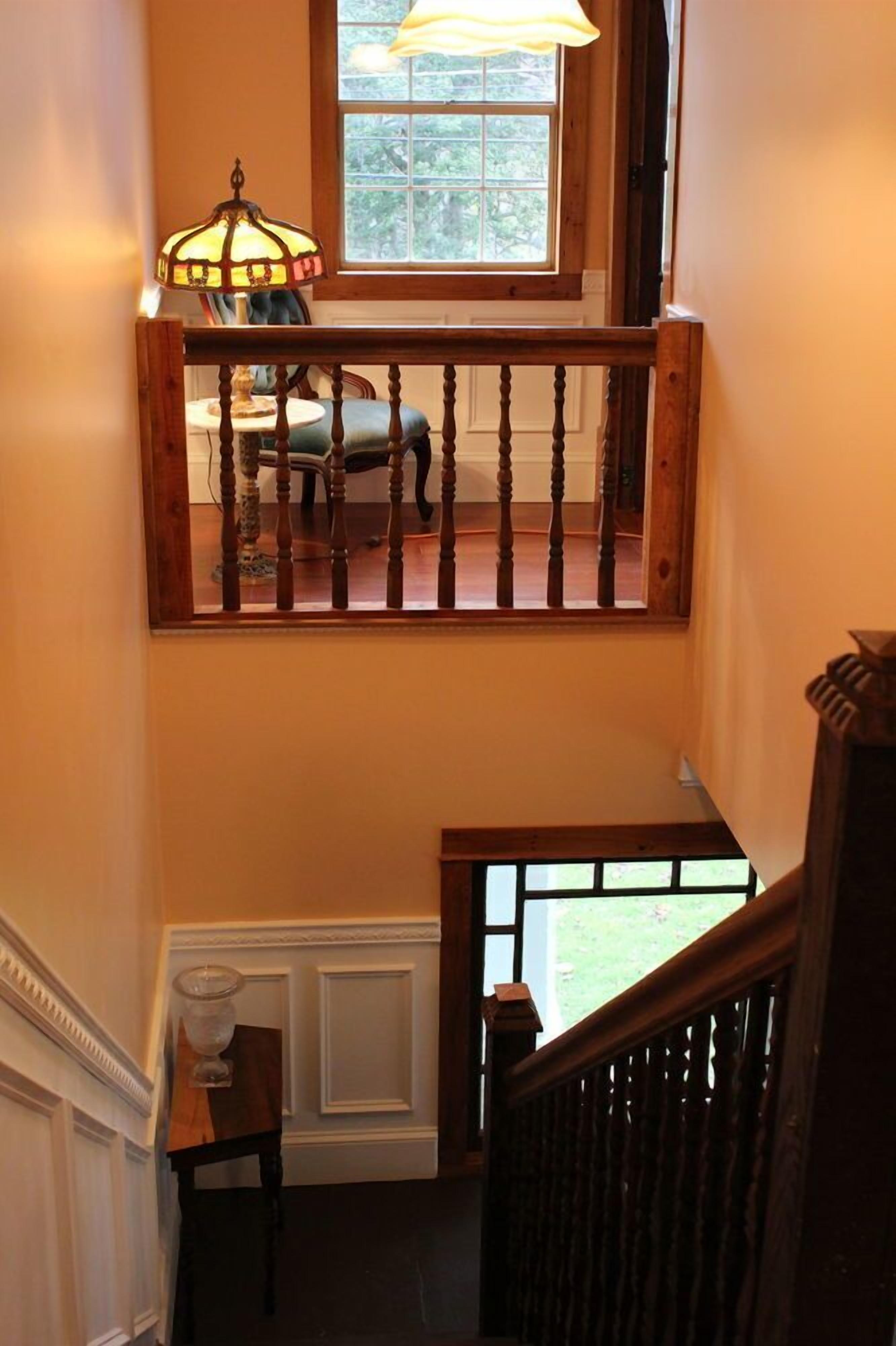 Un escalier avec une rampe en bois, une lampe et une vue sur une voiture à travers une fenêtre.