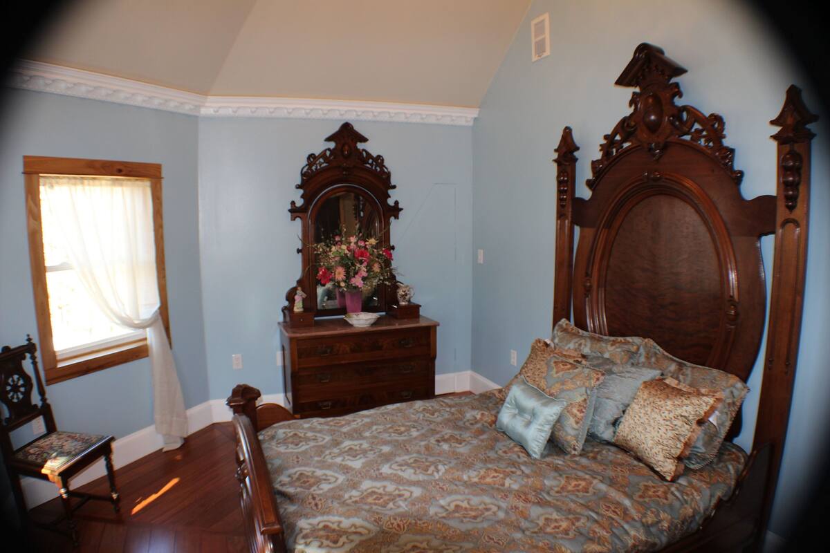 A bedroom with a wooden bed, a dresser, a mirror, and a chair.