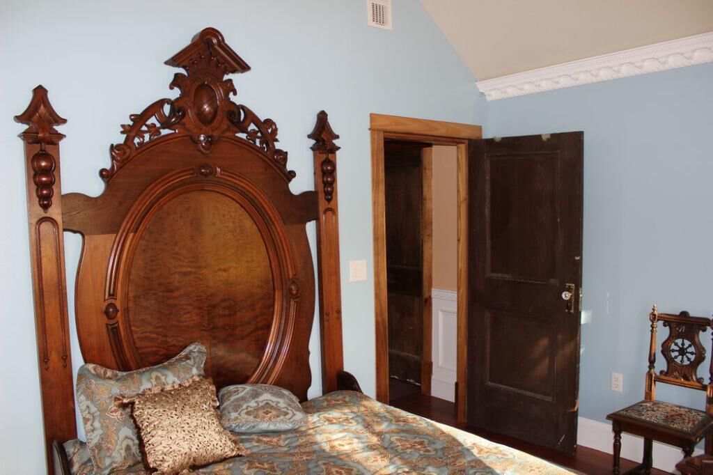 A bedroom with a large wooden bed, a wooden chair, and a dark wooden door.