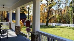 A covered porch with a stone column, a white fence, and a view of a grassy yard with trees. - Millsap-baker Estate (Damascus)