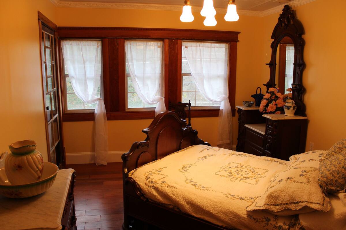 A room with a wooden bed, a dresser, a mirror, and a window with curtains.