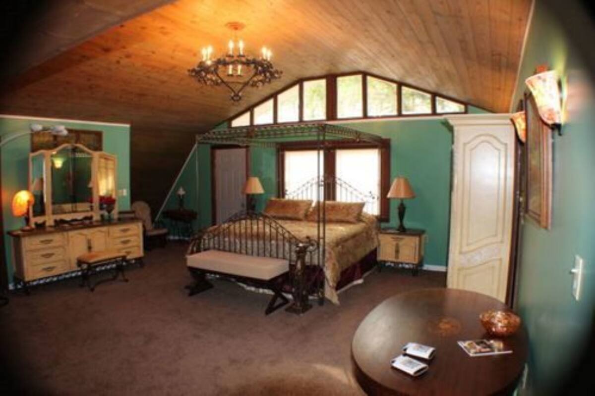 A bedroom with a four-poster bed, a dresser, a vanity, and a round table with a lamp.
