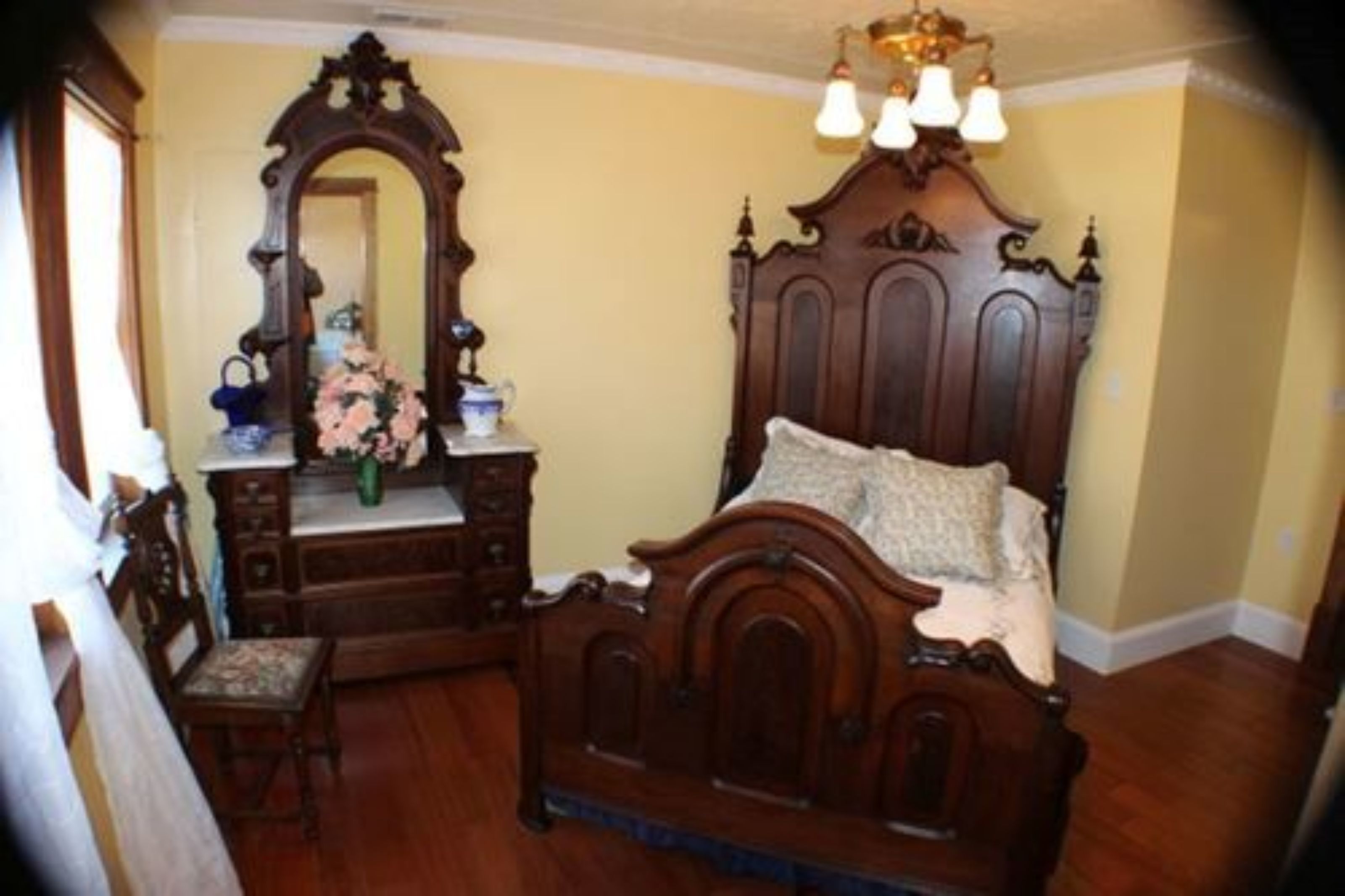 Un dormitorio con una cama de madera, un aparador, un espejo y una silla.
