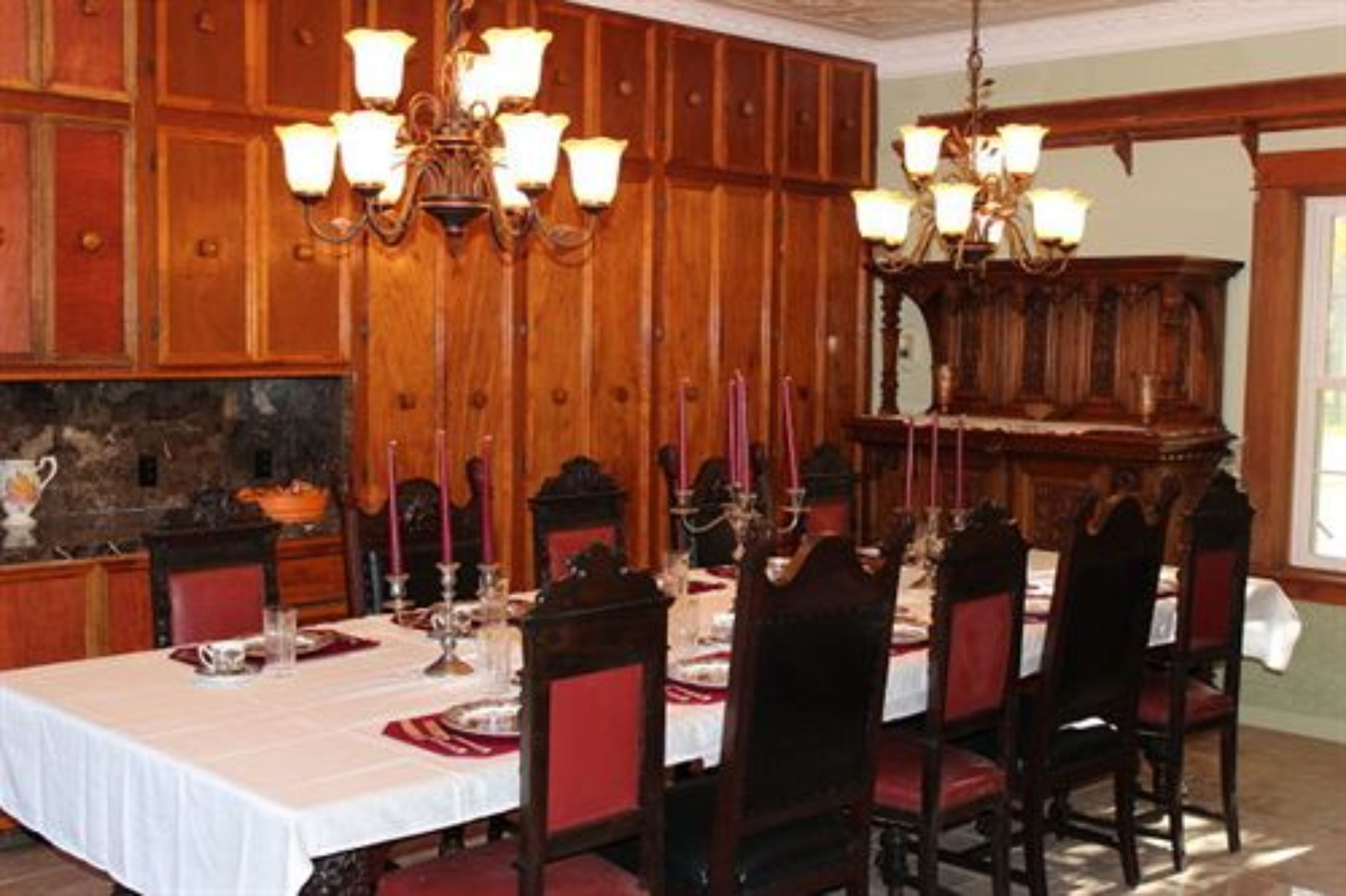 A dining room with a wooden paneled wall, a chandelier, and a table set for six.