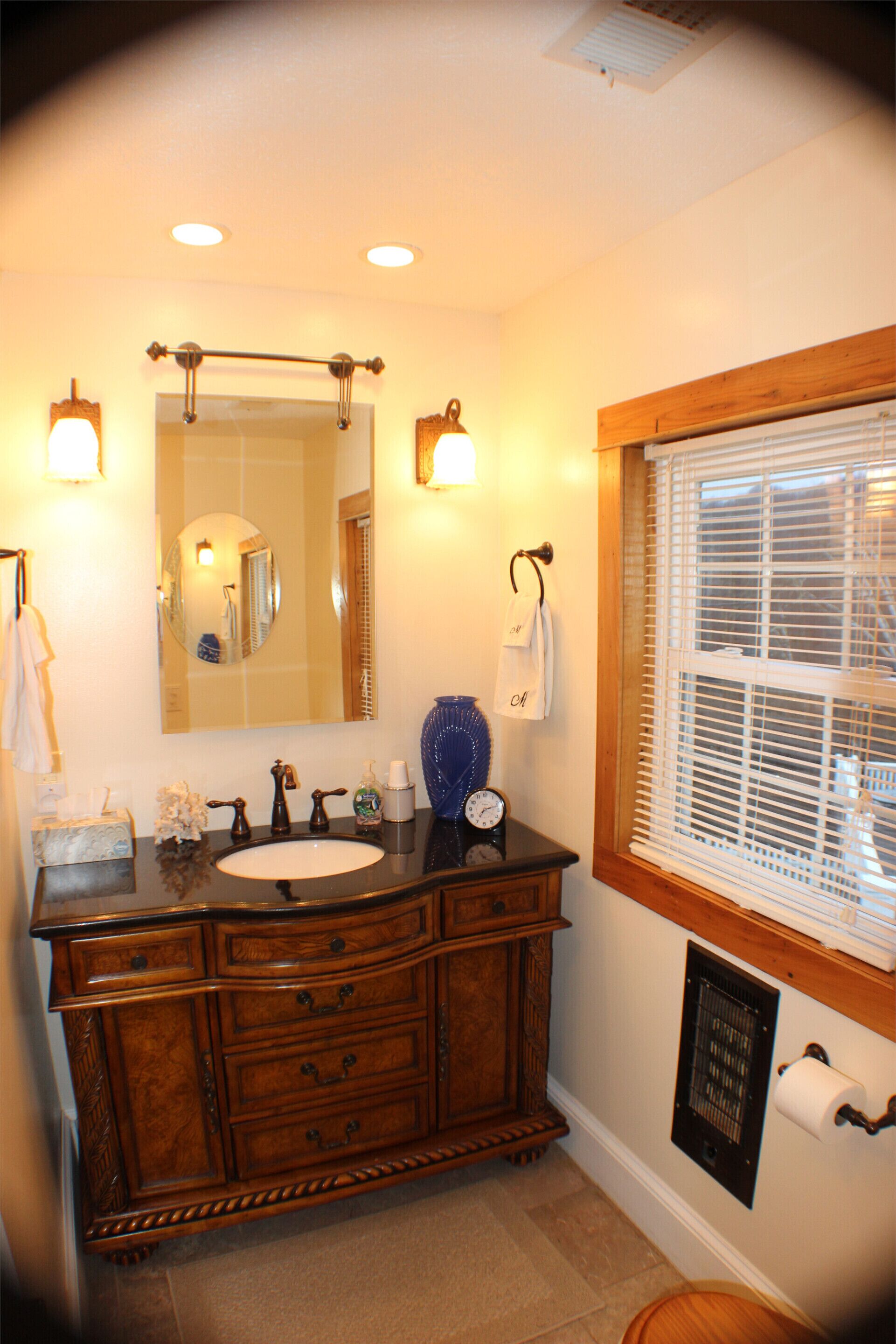 Une salle de bain avec un meuble-lavabo en bois, un miroir, un évier et une fenêtre avec des stores.