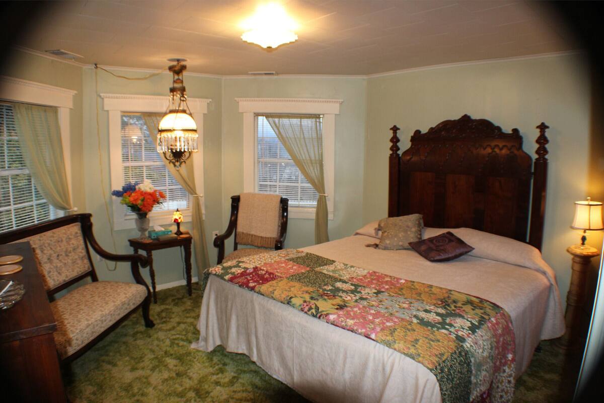 A bedroom with a large bed, a wooden headboard, a chair, a desk, and a chandelier.