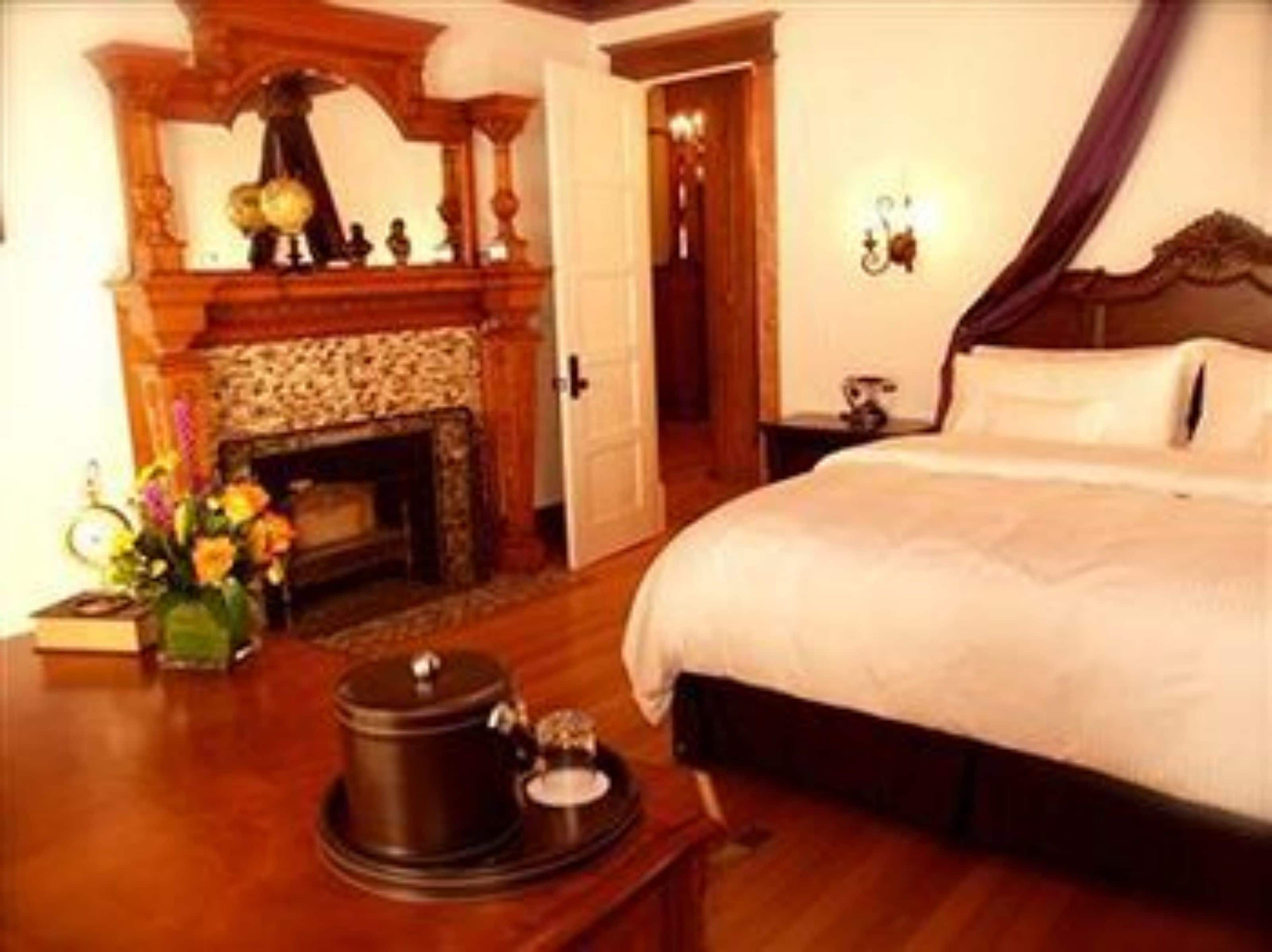 A hotel room with a large bed, a fireplace, a nightstand, and a vase of flowers.