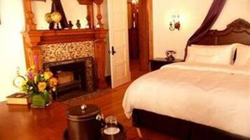 A hotel room with a large bed, a fireplace, a nightstand, and a vase of flowers.