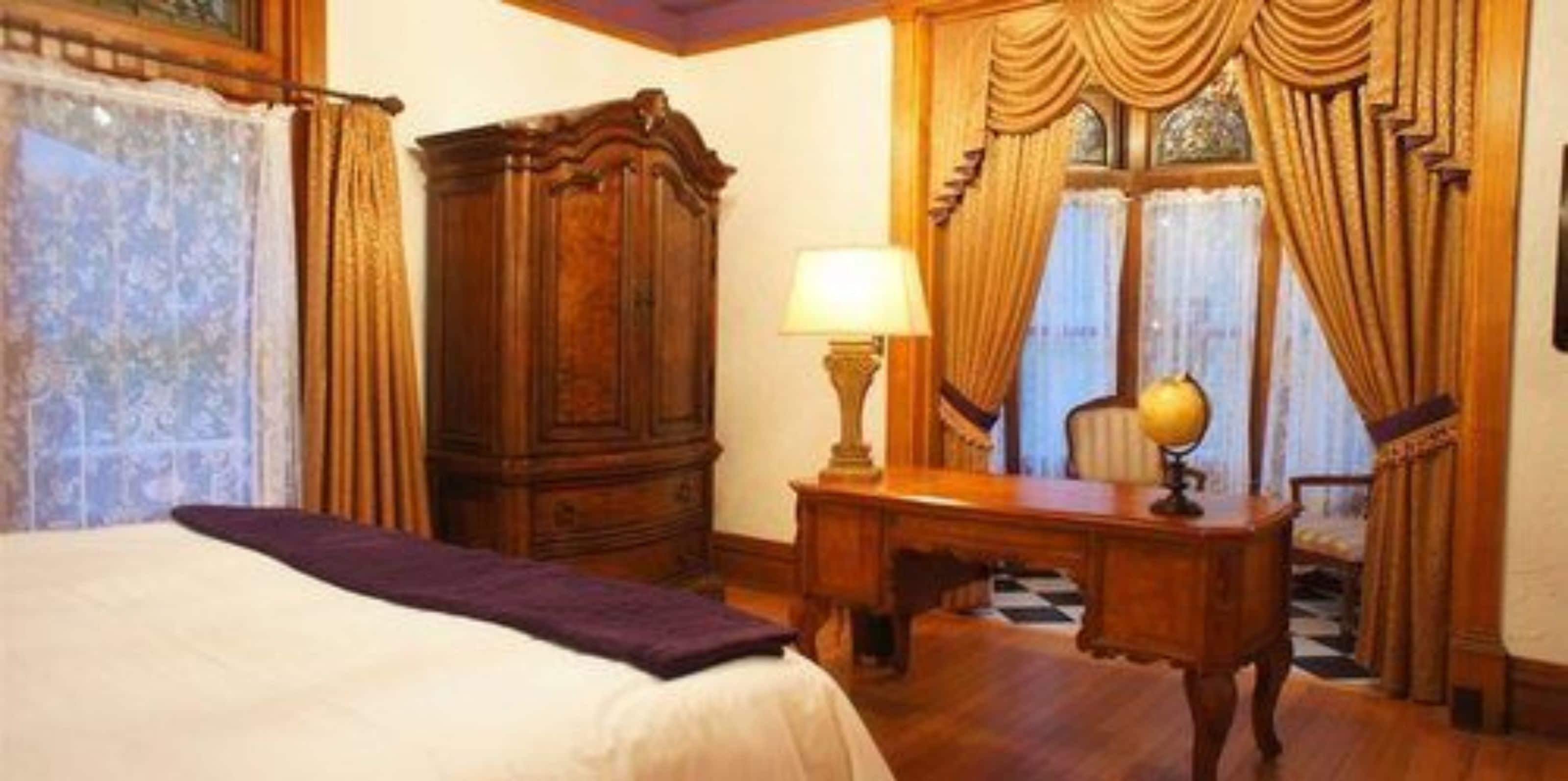 Een hotelkamer met een bed, een houten bureau, een lamp en gordijnen.
