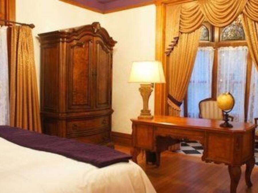 Een hotelkamer met een bed, een houten bureau, een lamp en gordijnen.