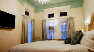 A hotel room with a bed, curtains, a chandelier, and a television.
