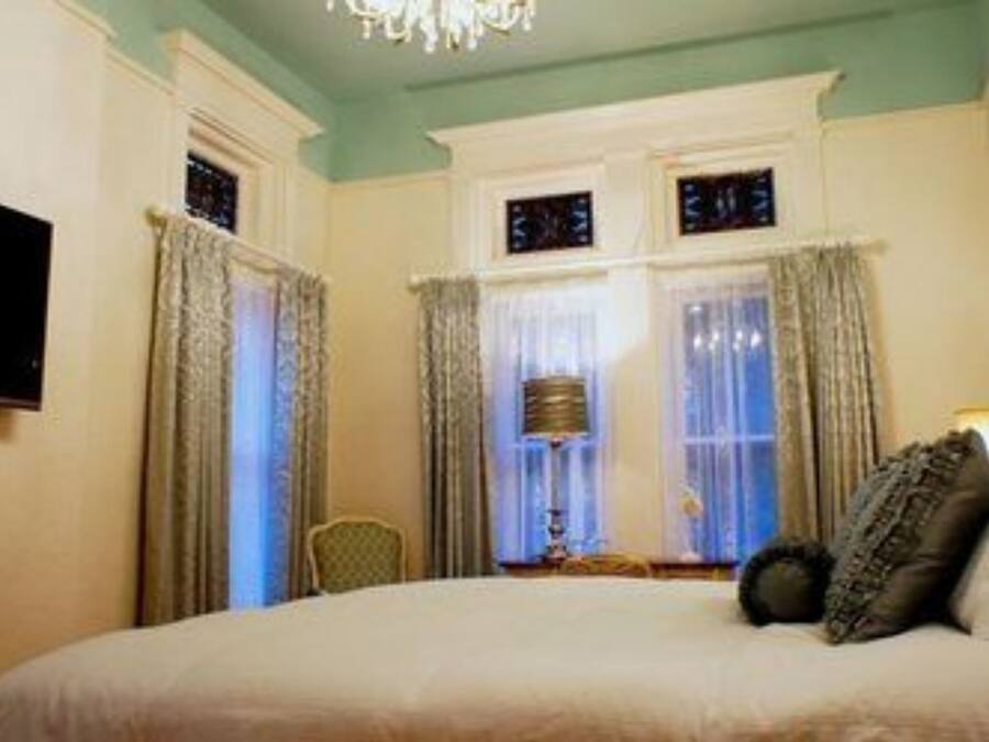 A hotel room with a bed, curtains, a chandelier, and a television.