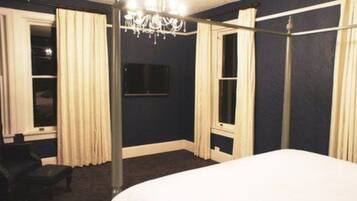 A bedroom with a large bed, a chandelier, and curtains on the windows.