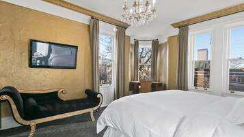 Ett hotellrum med en stor säng, en tv som är monterad på väggen, en bänk och en kristallkrona.