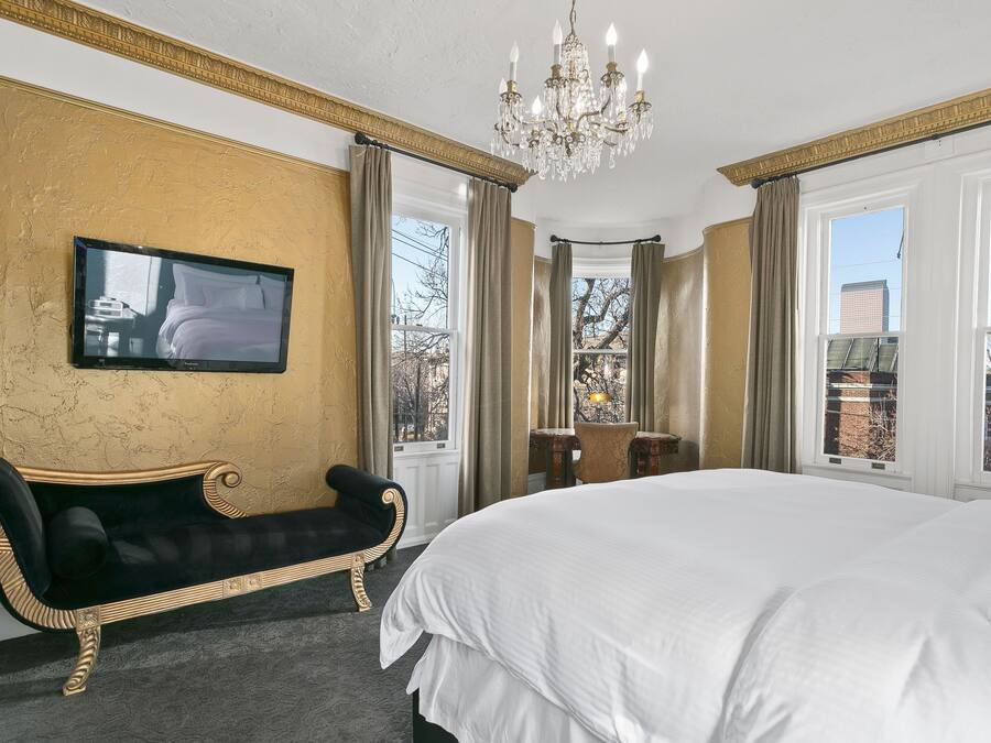 Ett hotellrum med en stor säng, en tv som är monterad på väggen, en bänk och en kristallkrona.