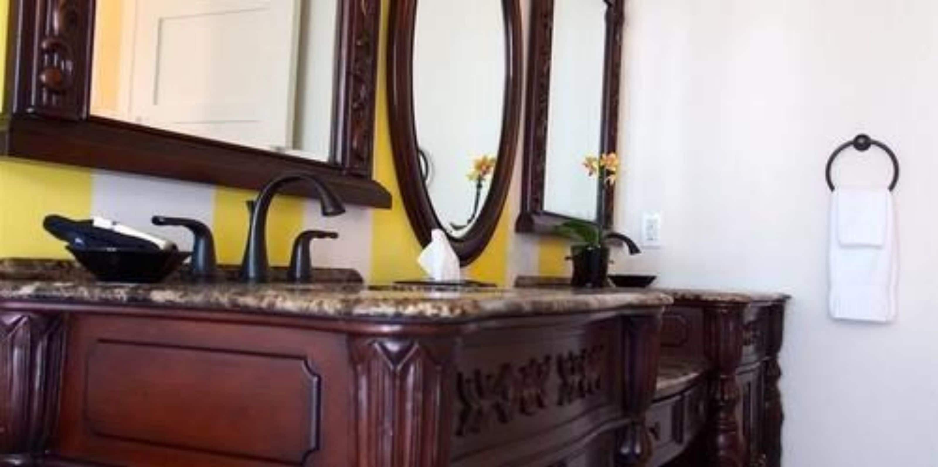 A bathroom with a wooden vanity, a mirror, a towel rack, and a potted plant.