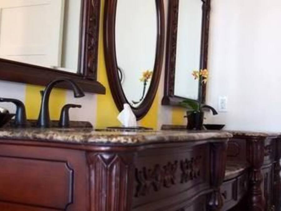 A bathroom with a wooden vanity, a mirror, a towel rack, and a potted plant.