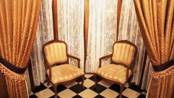 Una habitación con dos sillas iguales, dispuestas frente a frente, un suelo a cuadros y cortinas con un diseño estampado.