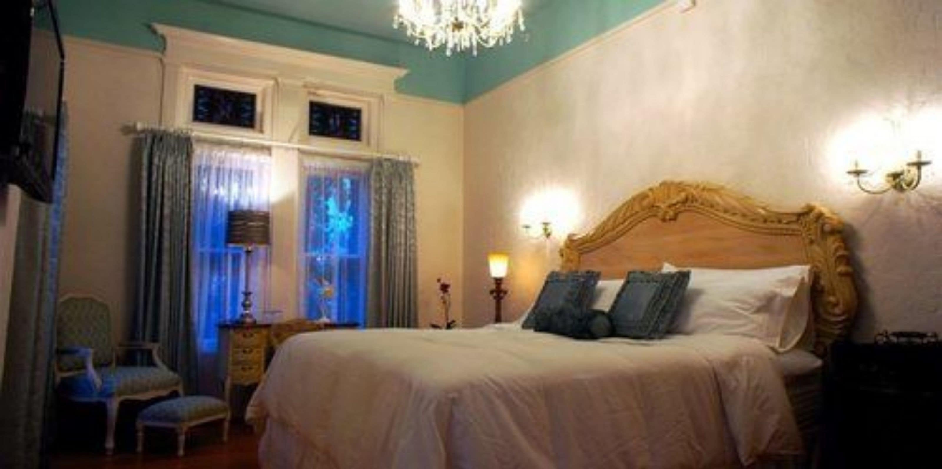 A bedroom with a large bed, a chandelier, and curtains.