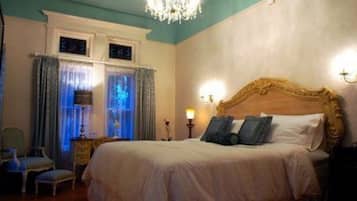 A bedroom with a large bed, a chandelier, and curtains.