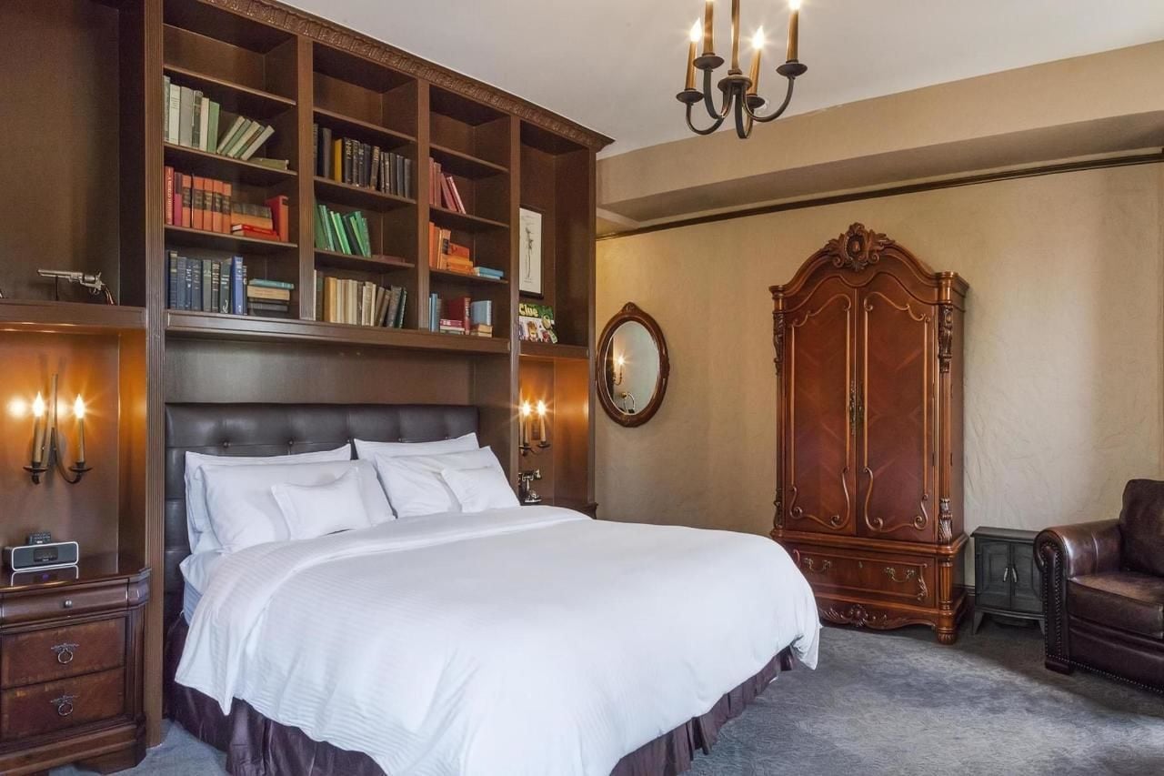 Une chambre avec un grand lit, une bibliothèque en bois, une armoire et un fauteuil en cuir.