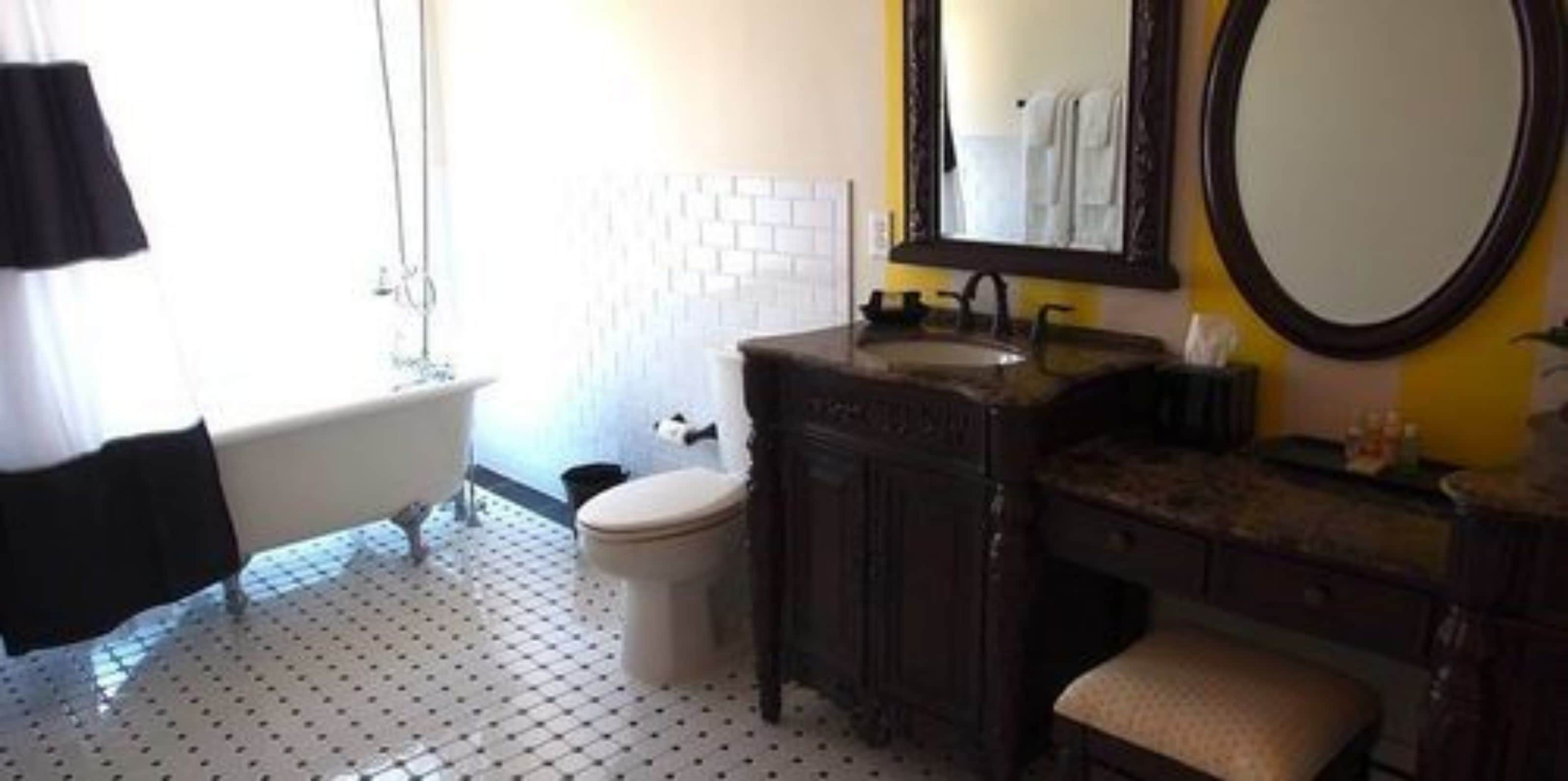 Een badkamer met een wit toilet, een bad, een wastafel met spiegel en een vloer met een patroon.