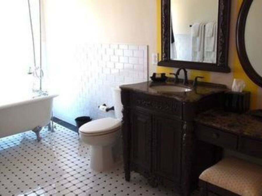 Een badkamer met een wit toilet, een bad, een wastafel met spiegel en een vloer met een patroon.