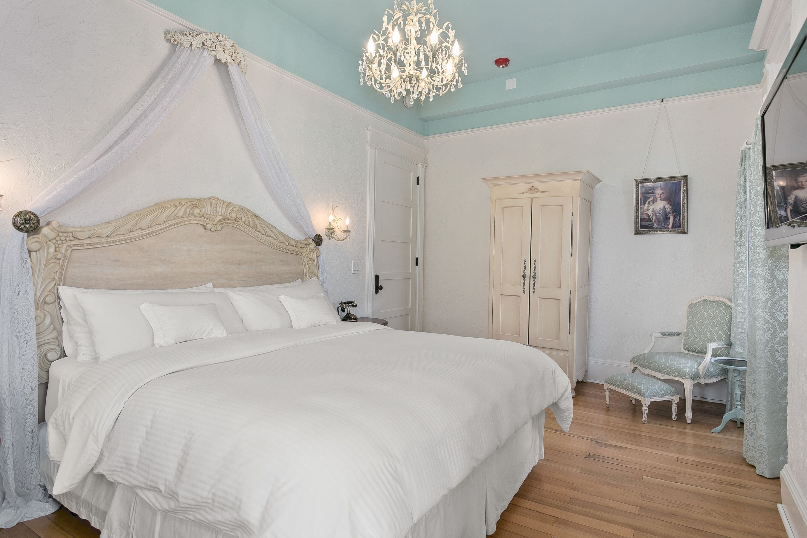 Une chambre à coucher avec un lit à baldaquin, un lustre, une armoire et une petite table avec une chaise.