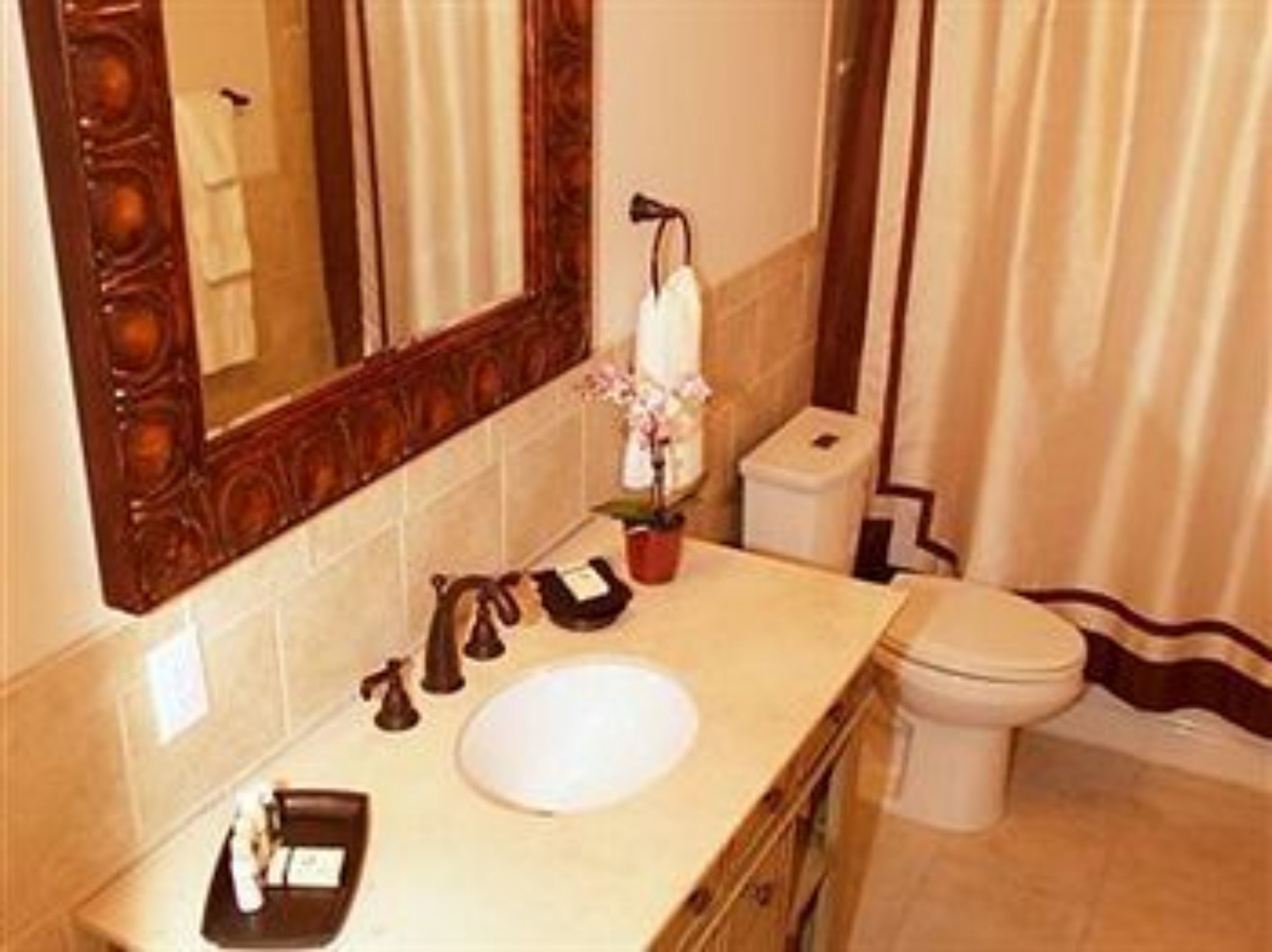 A bathroom with a wooden vanity, a large mirror, a white sink, a toilet, and a small trash bin.