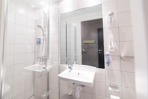 A modern bathroom with a glass shower enclosure, a white sink, and a hairdryer mounted on the wall.