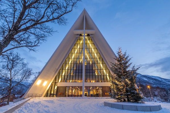 A modern building with a triangular facade and large windows, surrounded by snow and trees.