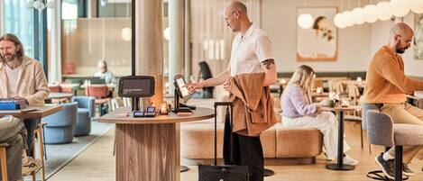 Un moderno vestíbulo de hotel con un quiosco de auto-check-in, zonas de estar y un gran pilar.