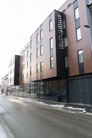 A modern hotel with a black and brown facade, large windows, and a visible name sign.