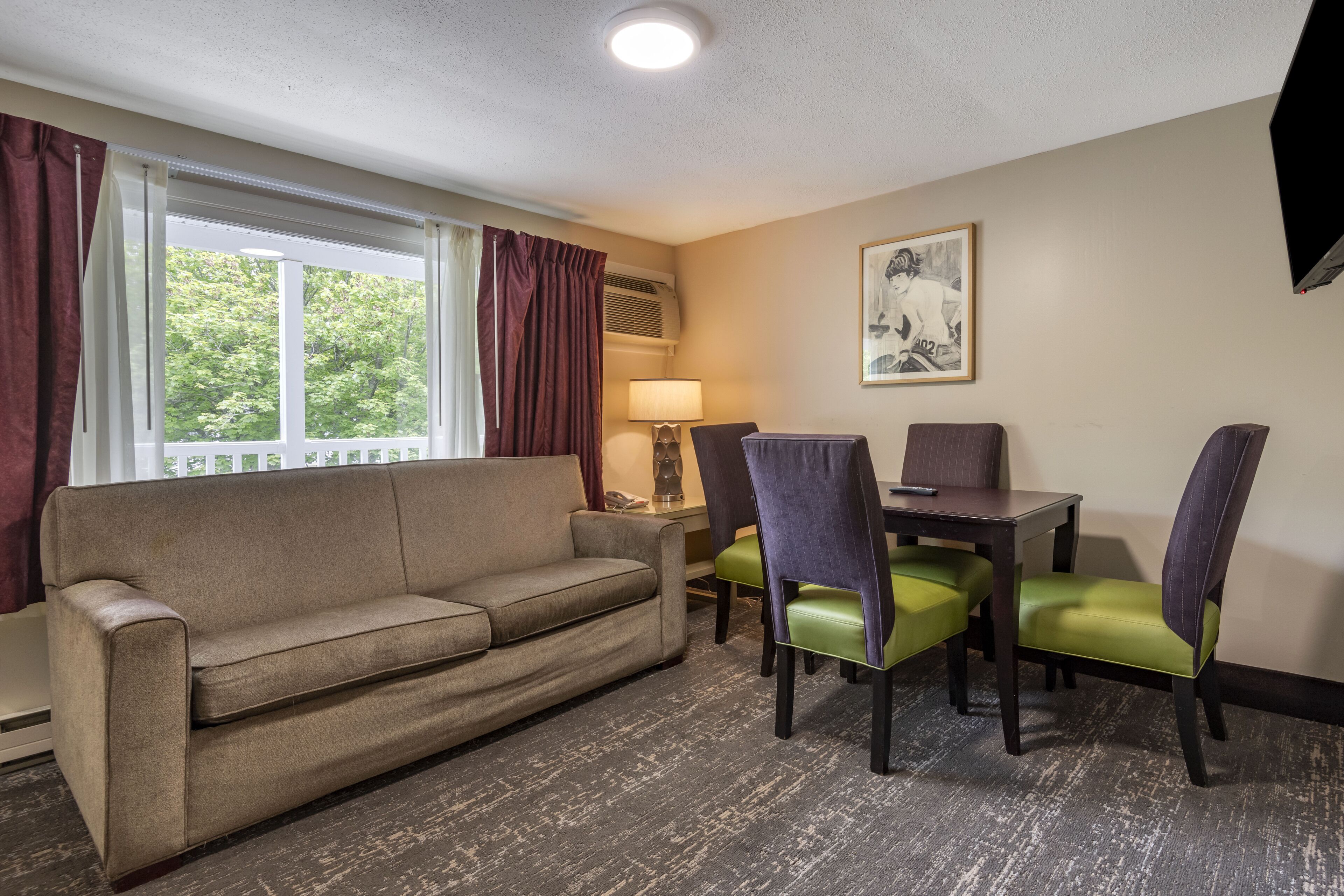 A hotel room with a sofa, two chairs, a table, and a lamp.