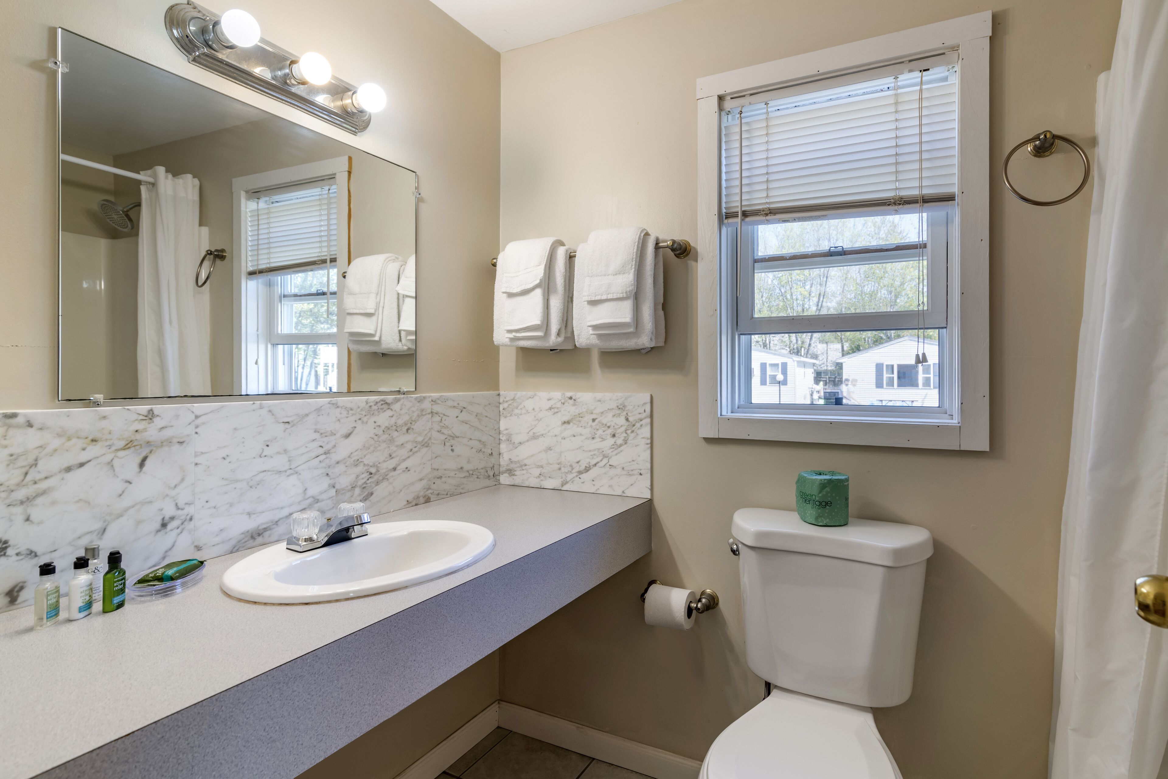A bathroom with a marble countertop, a sink, a toilet, and a window with blinds.
