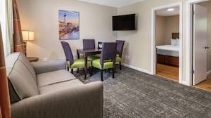 A hotel room with a sofa, dining table, chairs, a flat-screen TV, and a bed. - Anchor Inn and Cottages Wells-Ogunquit (Wells)
