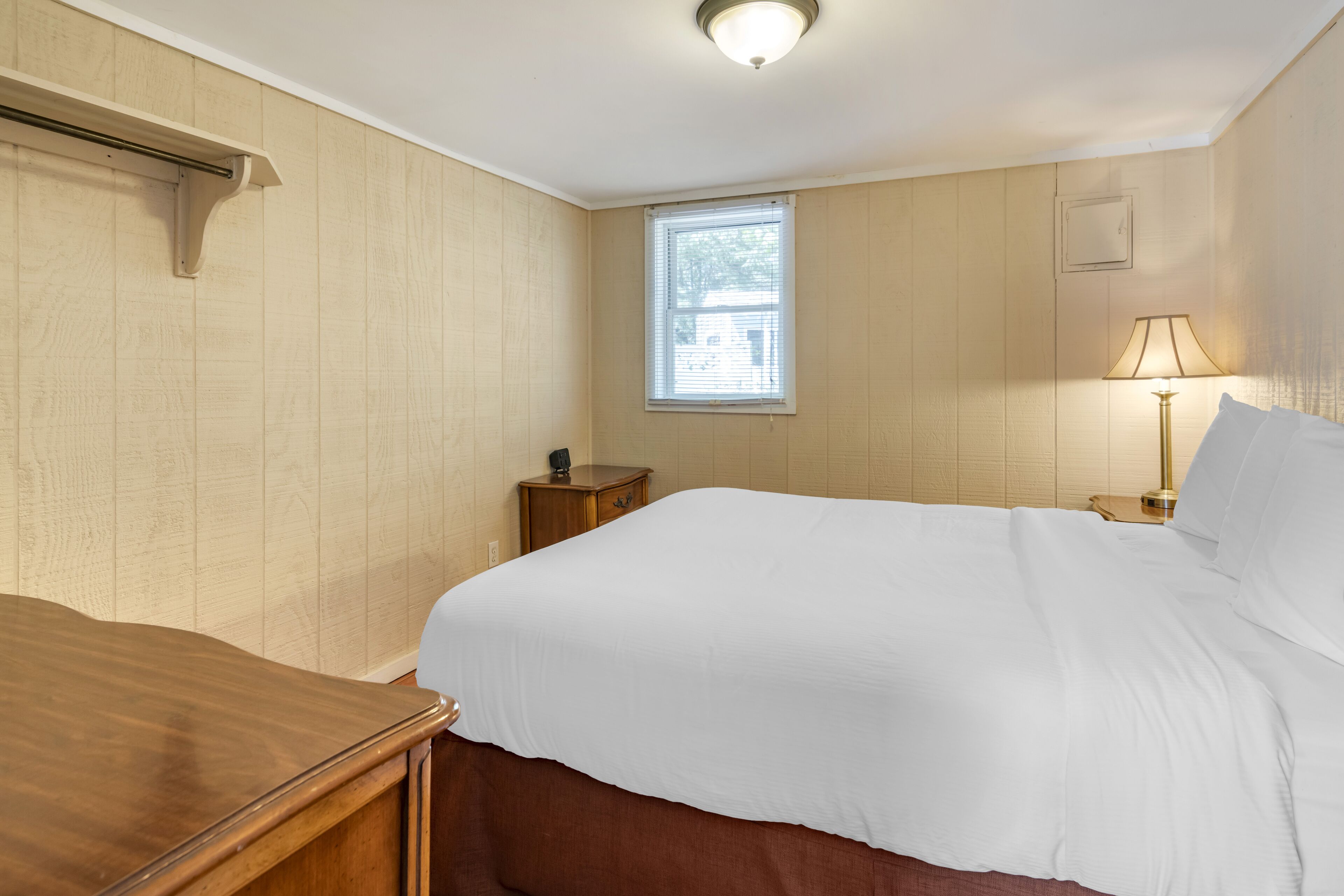 Une chambre à coucher avec un lit, une table de chevet, une lampe et une fenêtre.