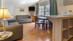 A compact living space with a sofa, a dining table with chairs, a lamp, a television, and a microwave. - Anchor Inn and Cottages Wells-Ogunquit (Wells)