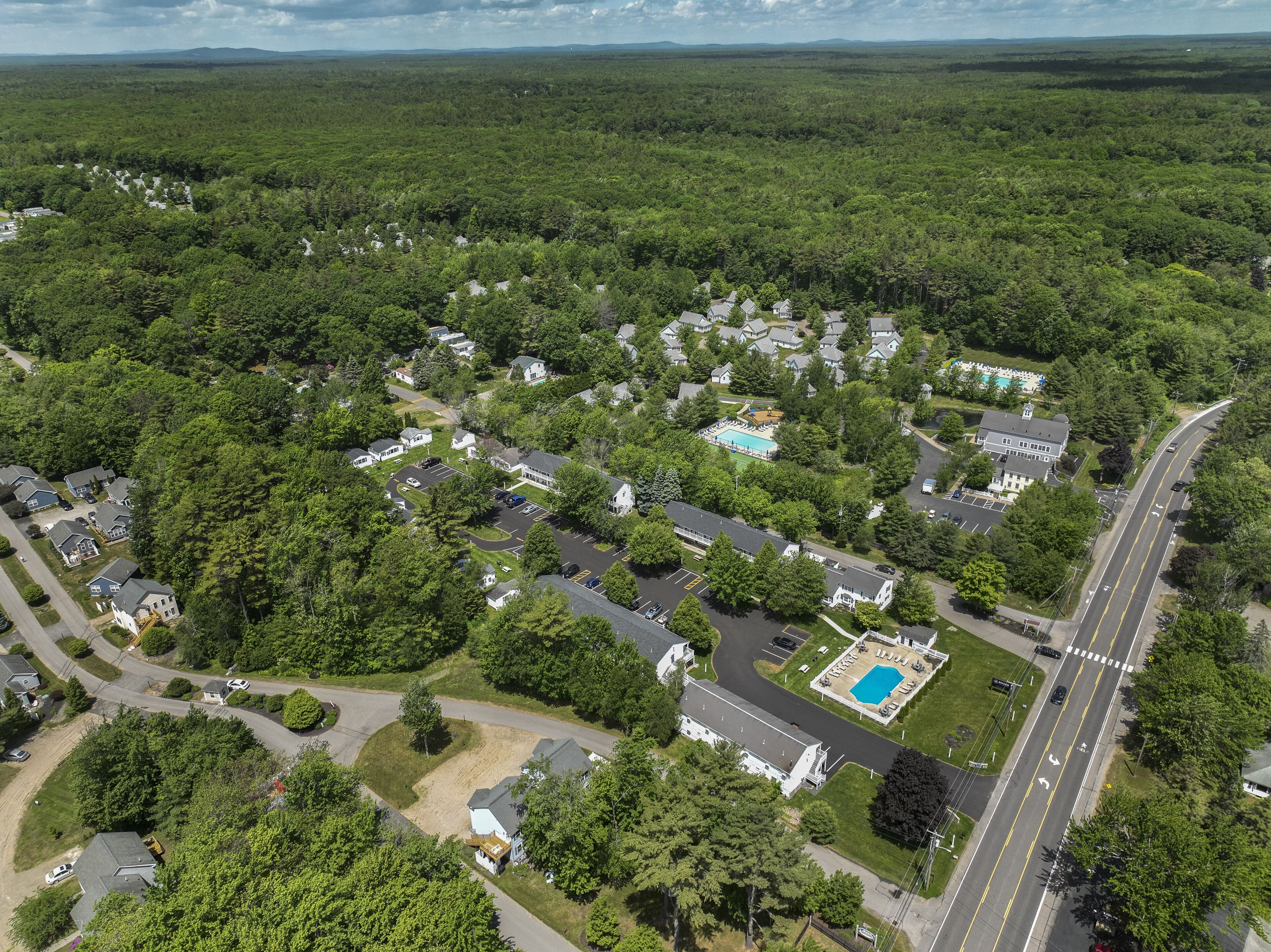 An aerial view of a residential area with houses, a swimming pool, and a road.