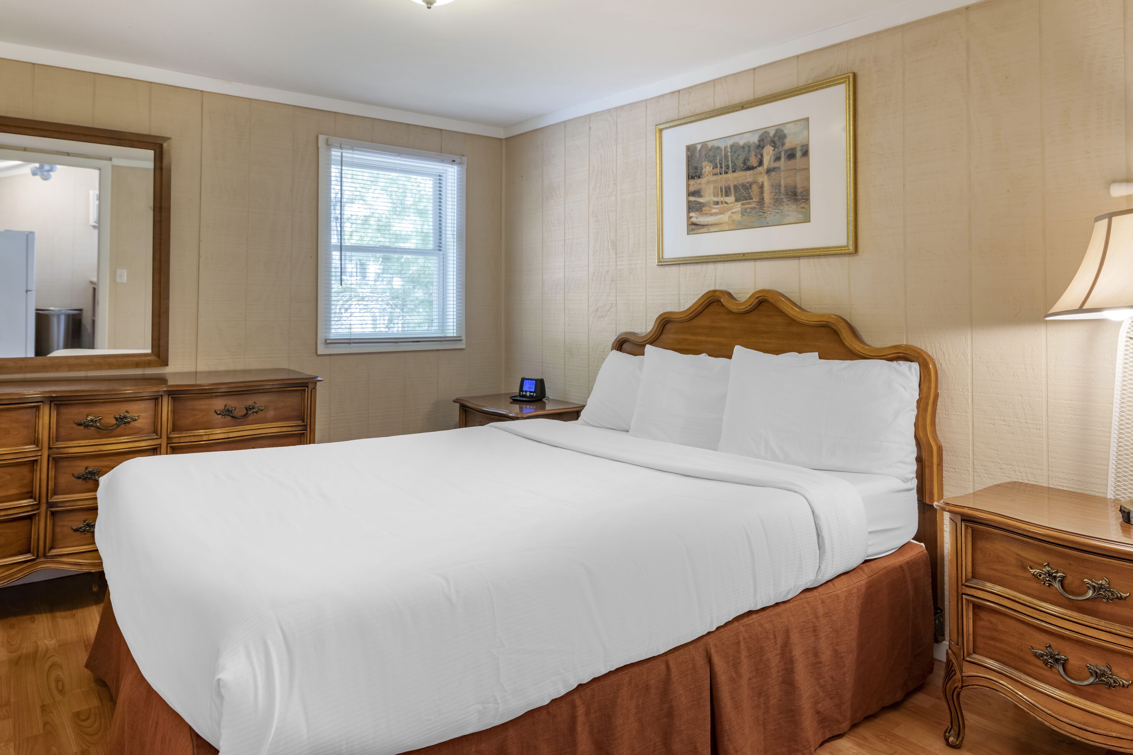 A neatly made bed in a room with wooden paneling, a bedside table with a lamp, and a framed picture on the wall.