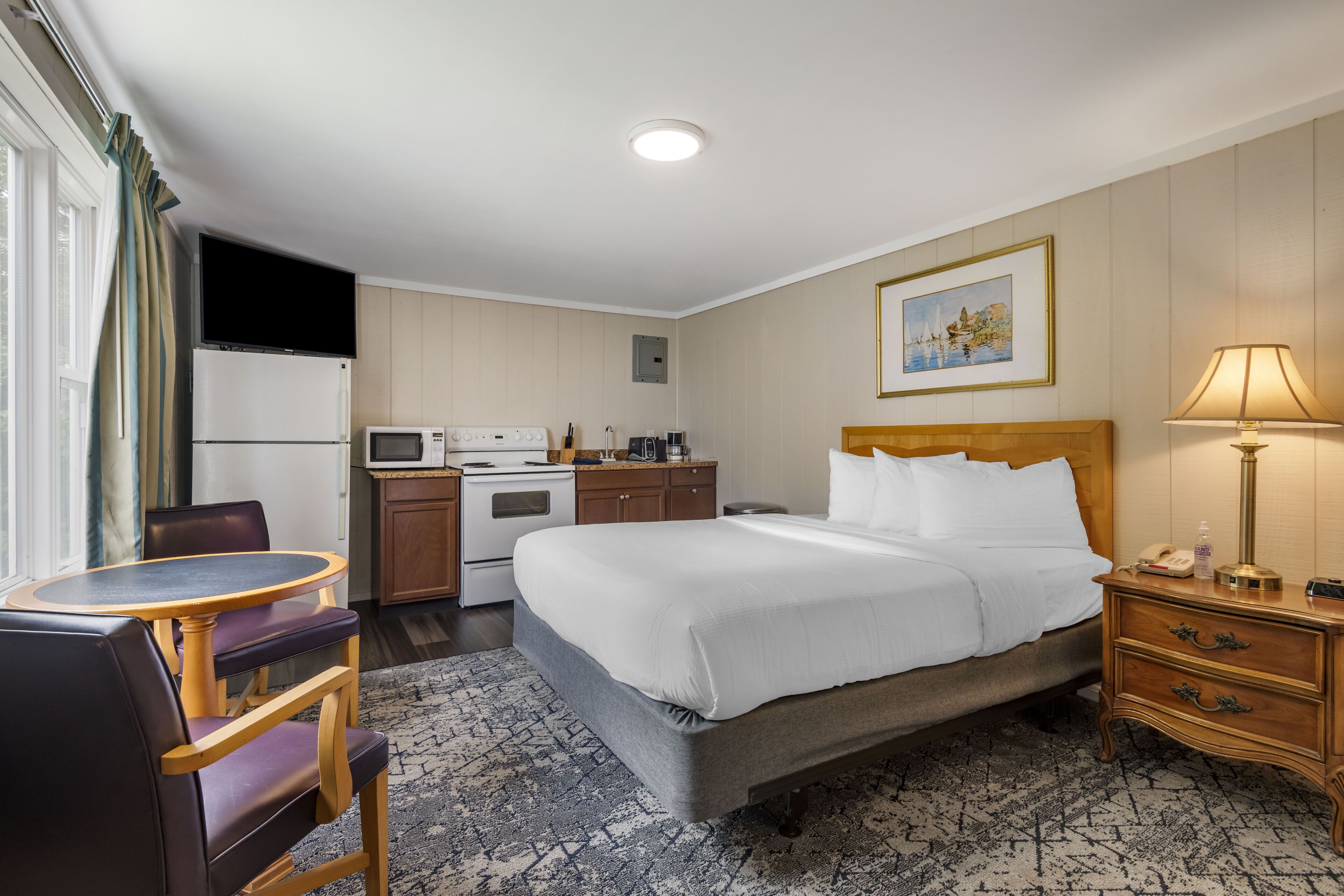Et hotelværelse med en seng, et natbord, en lampe og et lille skrivebord med stol.
