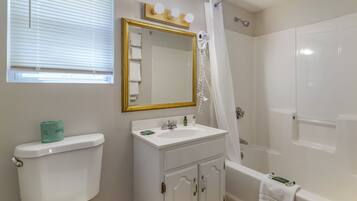 A bathroom with a toilet, sink, mirror, and shower.