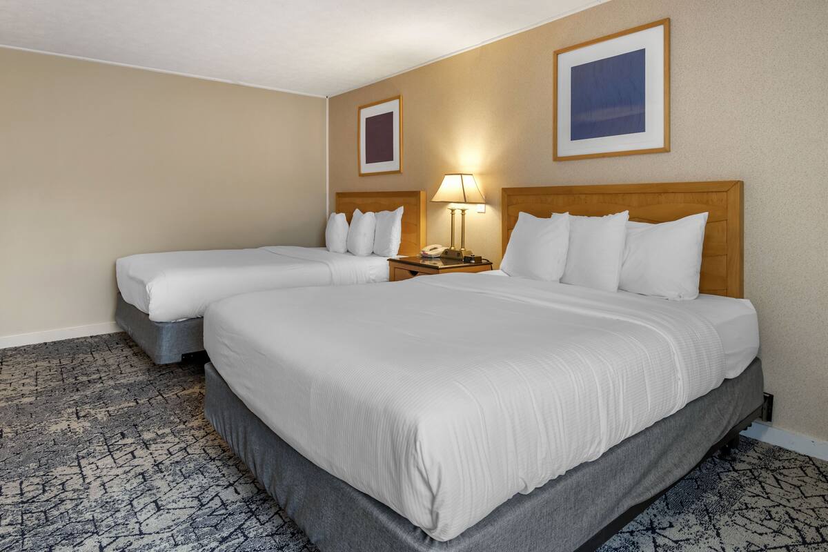A hotel room with two beds, a nightstand with a lamp, and two framed pictures on the wall.