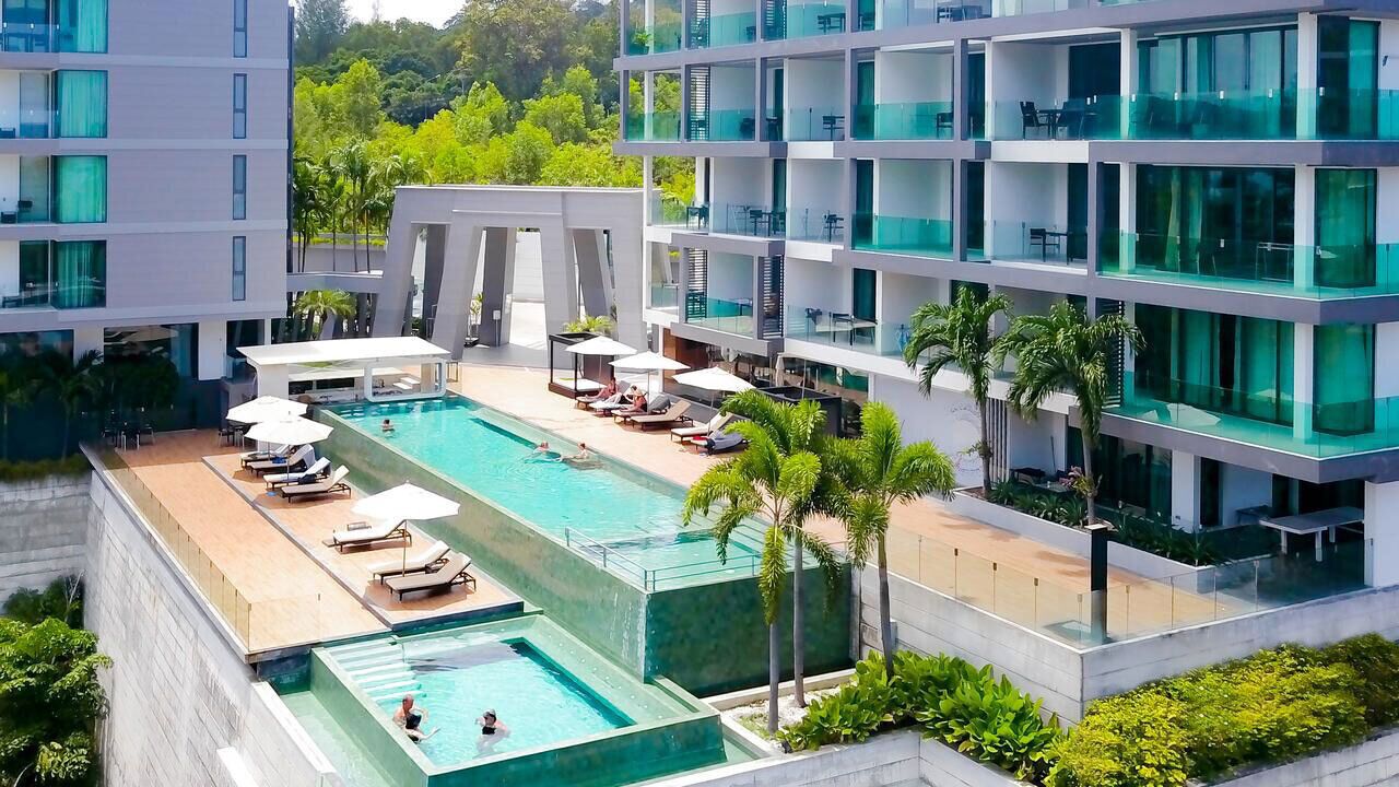 A modern hotel with a rooftop infinity pool, multiple balconies, and lush greenery.