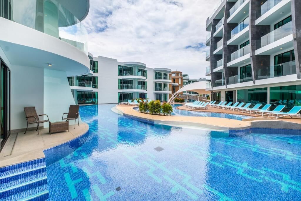 A modern hotel with a central swimming pool, lounge chairs, and a glass facade.