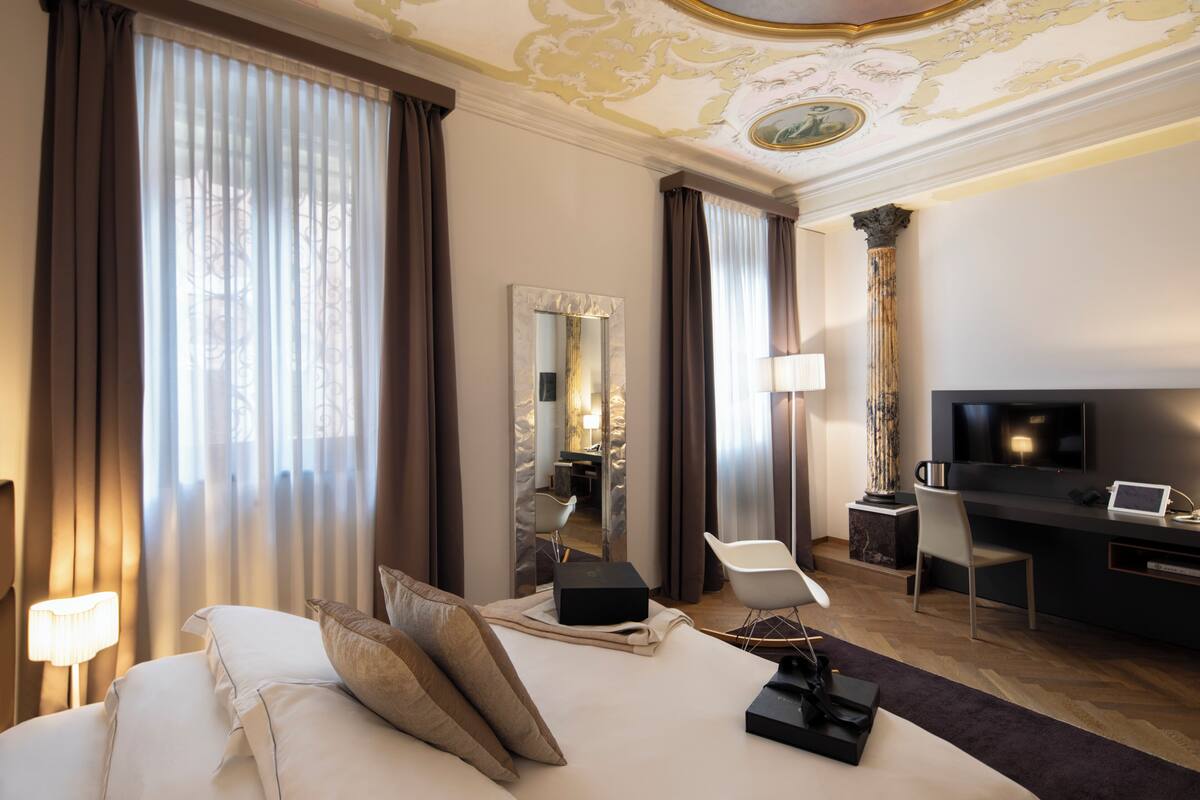 Una camera d'albergo con un letto grande, una scrivania con un portatile, una televisione e uno specchio.