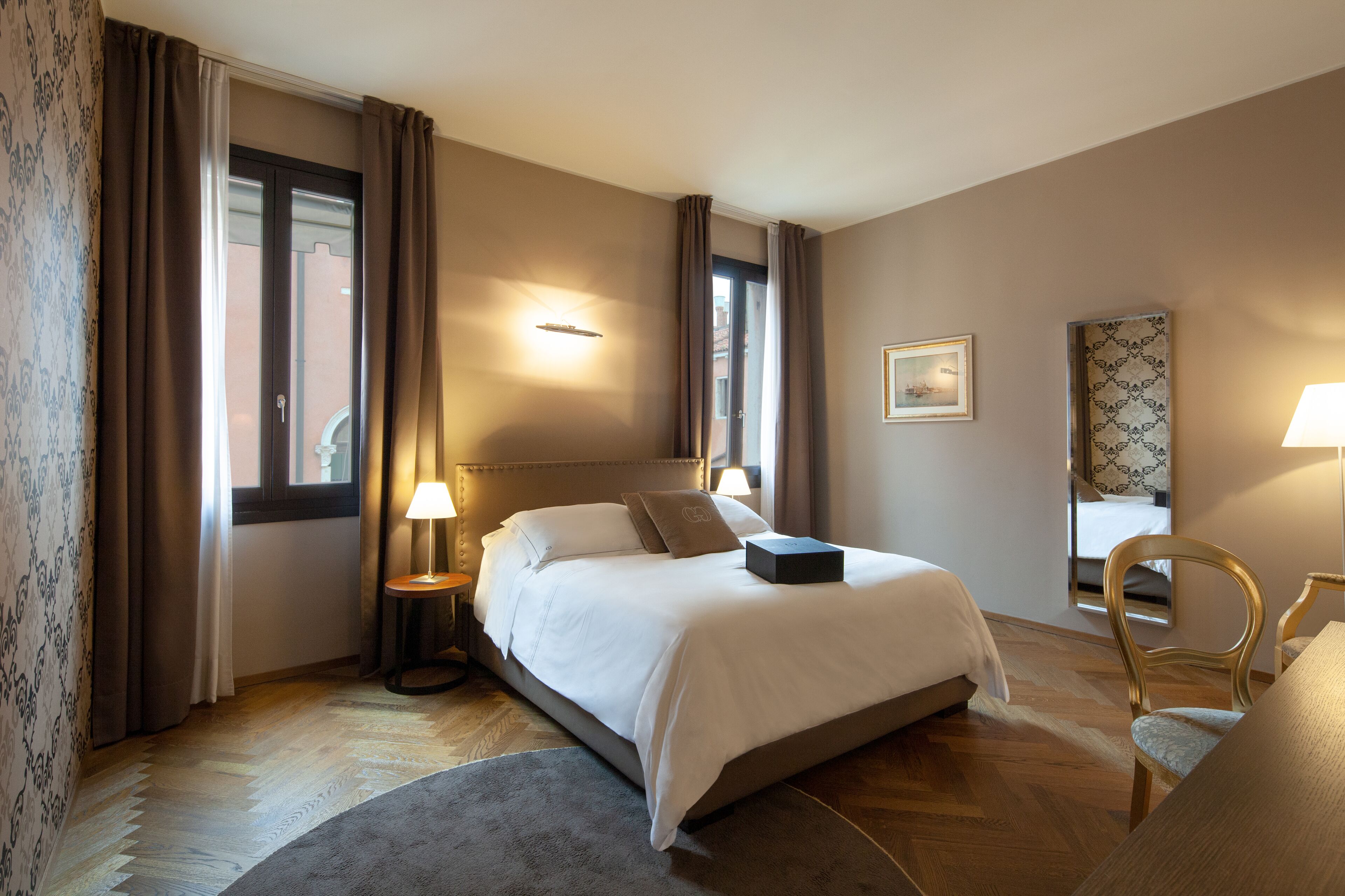A hotel room with a large bed, a desk, a chair, and a window with curtains.